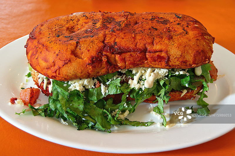 装满大豆“香肠”、土豆、生菜丝、豆腐奶油和豆腐奶酪的墨西哥面包三明治，在餐厅的盘子里供应图片素材