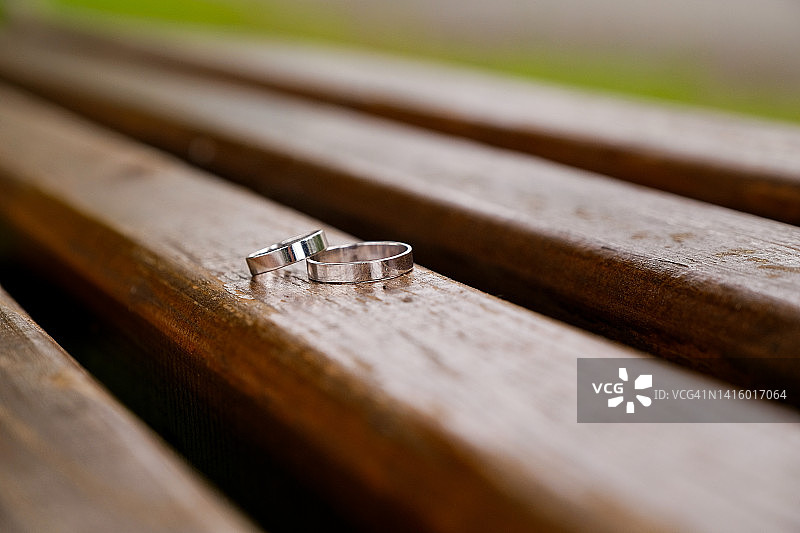 在公园旧木凳上，新娘和新郎的结婚戒指。这对新人的戒指由白金或银制成。婚礼主题。求婚。图片素材
