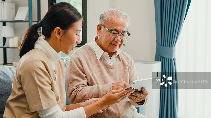 年轻亚裔专业护理员教老年男性在家用平板电脑图片素材