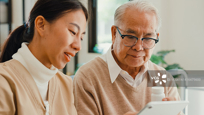 亚洲女护工指导老人使用平板电脑查看药物说明图片素材