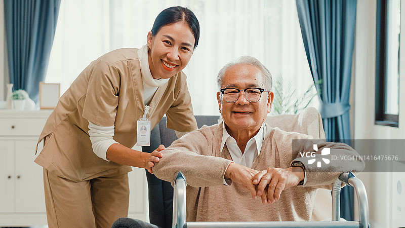 快乐的亚洲退休老人坐在翼背椅上，女护士握着他的手图片素材