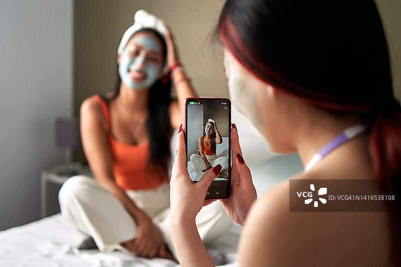 敷面膜的年轻女人用手机给朋友拍照的背影图片素材