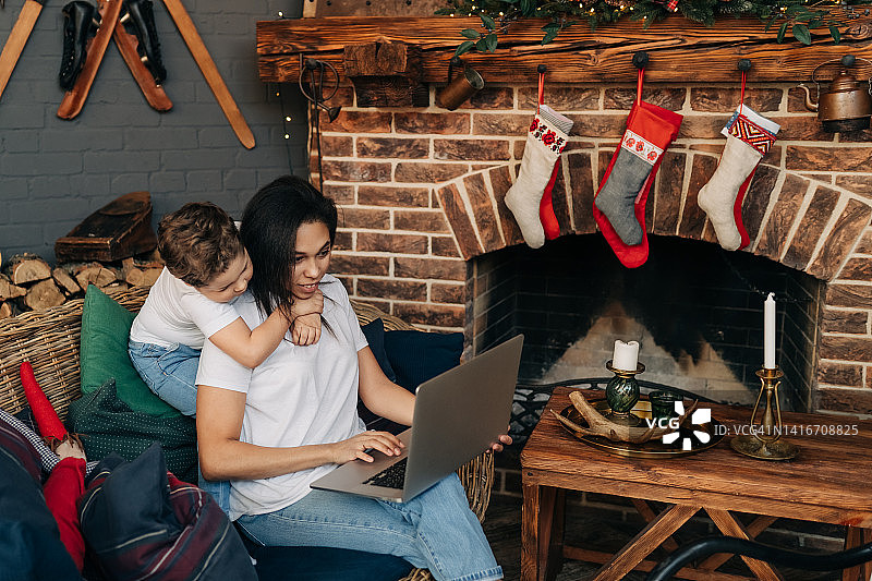 在家进行圣诞购物。一位女士在圣诞节期间与儿子坐在一起，手持信用卡和数码平板电脑图片素材