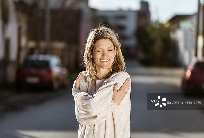 微笑的充满爱意的年轻女子拥抱自己图片素材