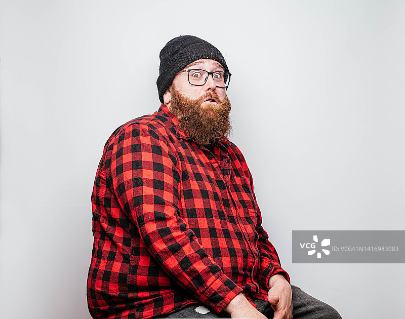 戴冬季无檐帽和格子衬衫的络腮胡男人做着滑稽的表情图片素材