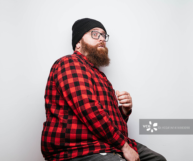 戴冬季无檐帽和格子衬衫的络腮胡男人做着滑稽的表情图片素材