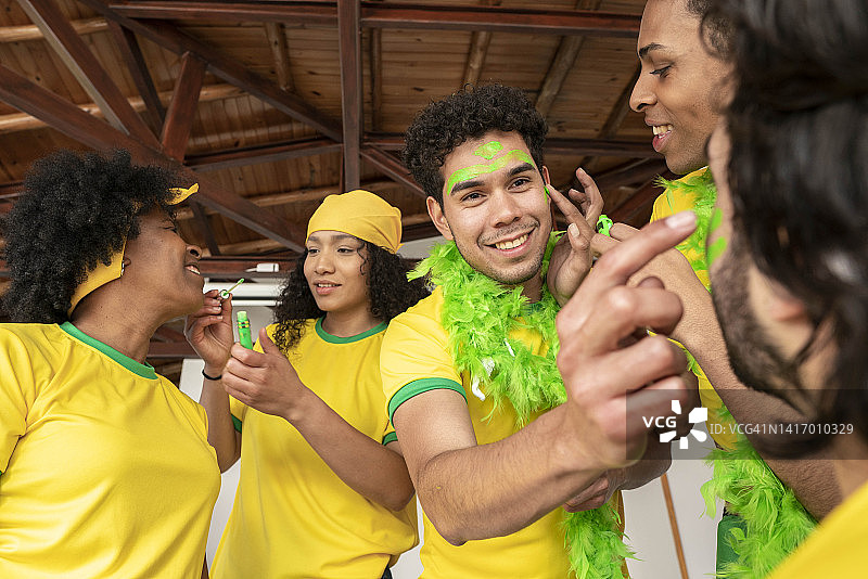 巴西足球队球迷在家里一起看比赛，并在脸上涂油彩图片素材