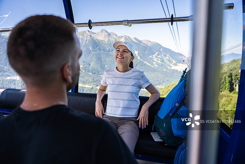 快乐的年轻女人背着背包乘坐缆车上山远足图片素材