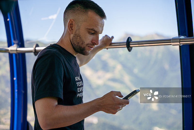 在缆车车厢内使用智能手机的成年男子图片素材