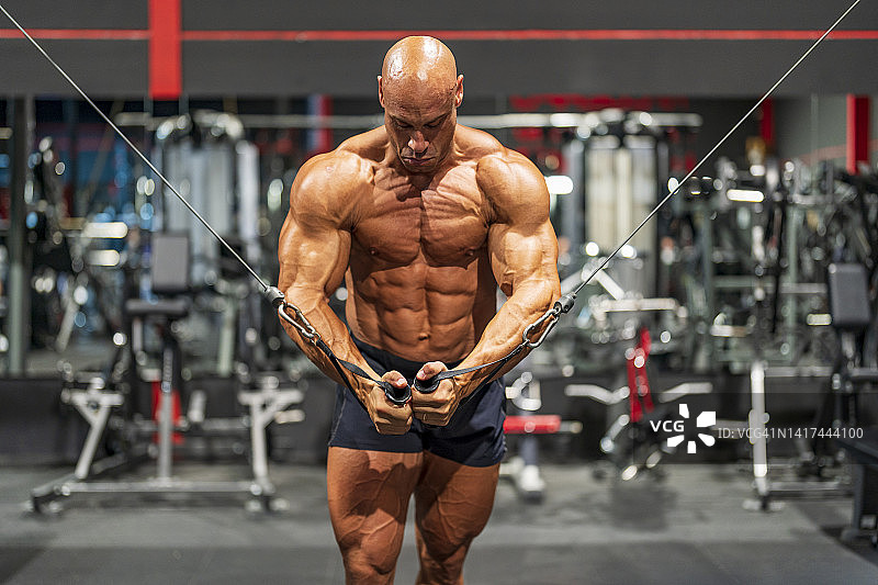 在健身房里通过拉索器械做胸部锻炼的裸着上身的健美运动员图片素材
