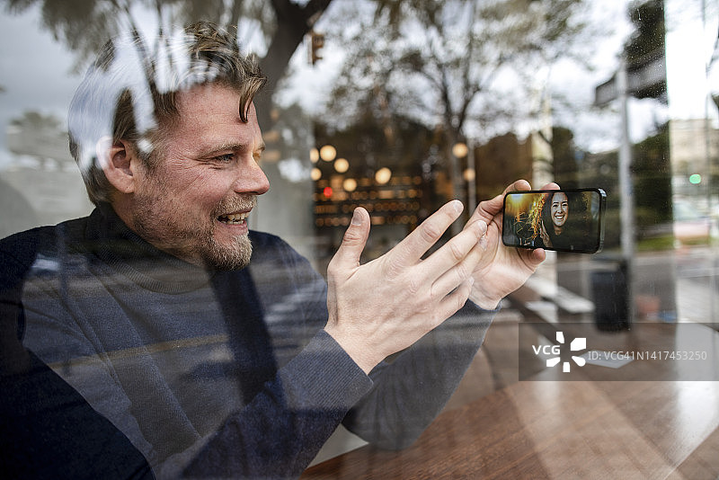 在咖啡馆用智能手机与女友视频通话的微笑商人图片素材
