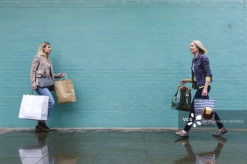 提着购物袋走在蓝色墙边湿滑人行道上的女性图片素材
