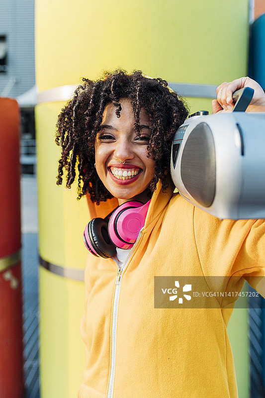 快乐的女人肩扛手提音响站在黄色管道前图片素材