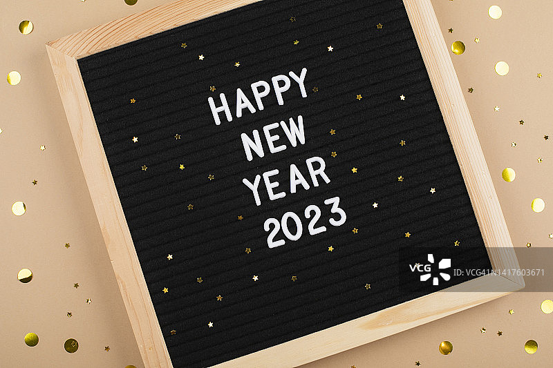2023新年快乐字母板。俯视图。米色背景与星星纸屑。贺卡图片素材