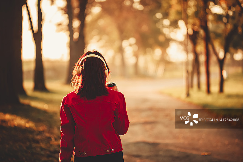 在秋天的公园里喝着咖啡行走的年轻女人图片素材