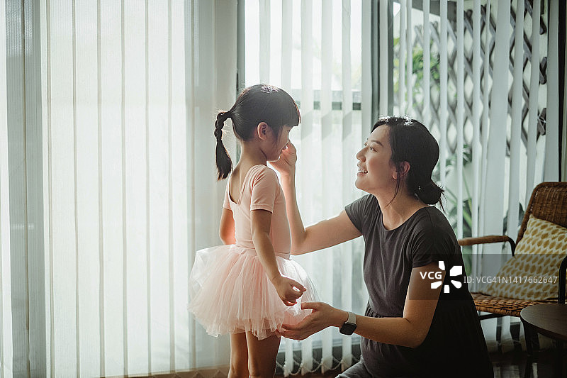 年轻的亚洲孕妇为女儿准备芭蕾舞课，给女儿穿上粉红色的芭蕾舞裙和芭蕾舞短裙。爱好和兴趣。家庭生活方式。母女时刻。爱、关怀和亲情概念图片素材