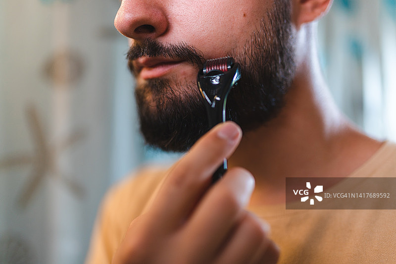 在浴室镜前用滚轮按摩胡须的年轻光头男子特写图片素材