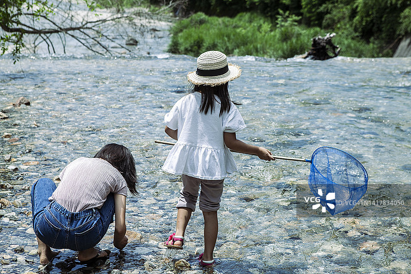 可爱的小女孩用网在小溪里抓鱼图片素材