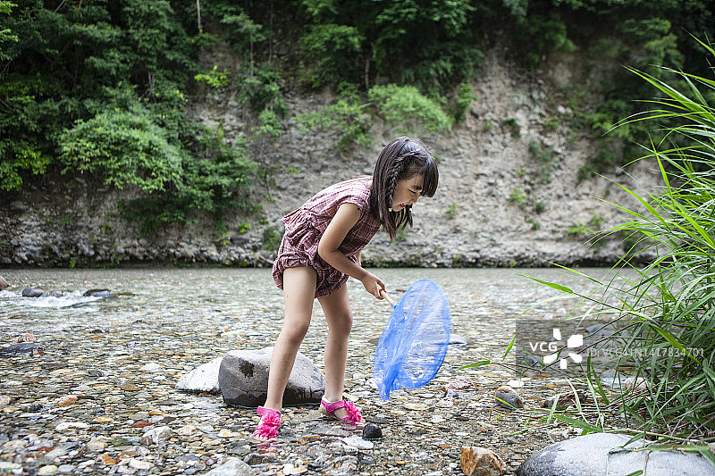 可爱的小女孩用网在小溪里抓鱼图片素材