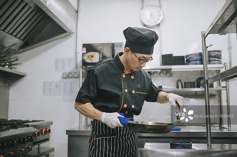 亚洲厨师在商业厨房准备食材，用夹子夹起对虾图片素材