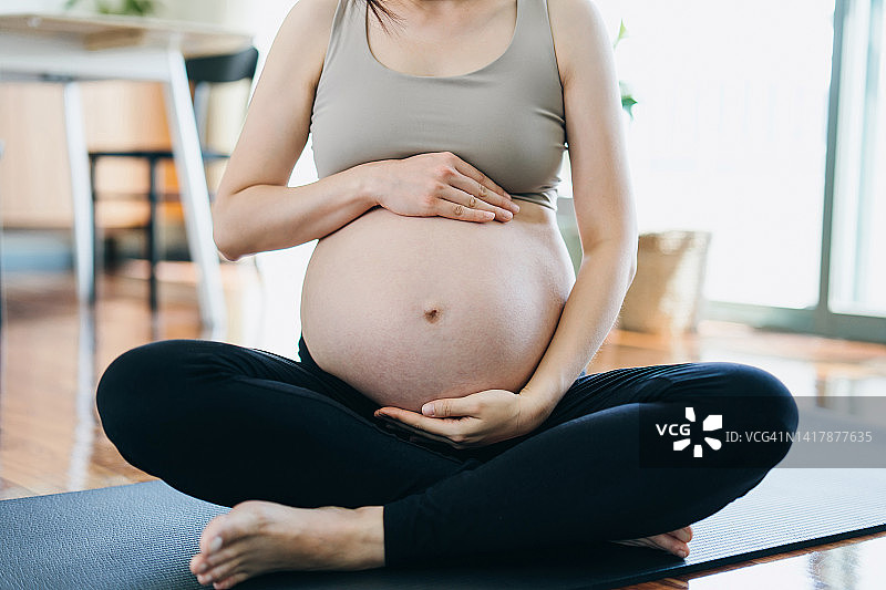 年轻孕妇居家锻炼爱抚腹部特写图片素材