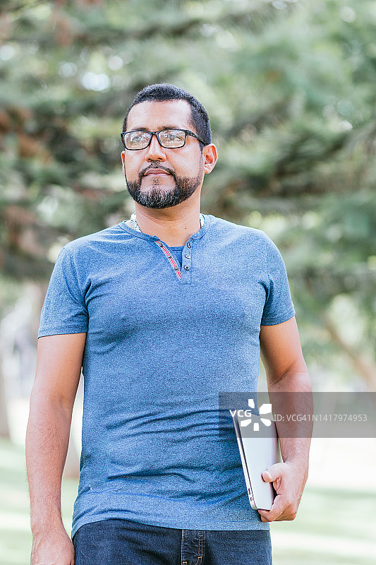 携带笔记本电脑穿过公园的英俊商人图片素材