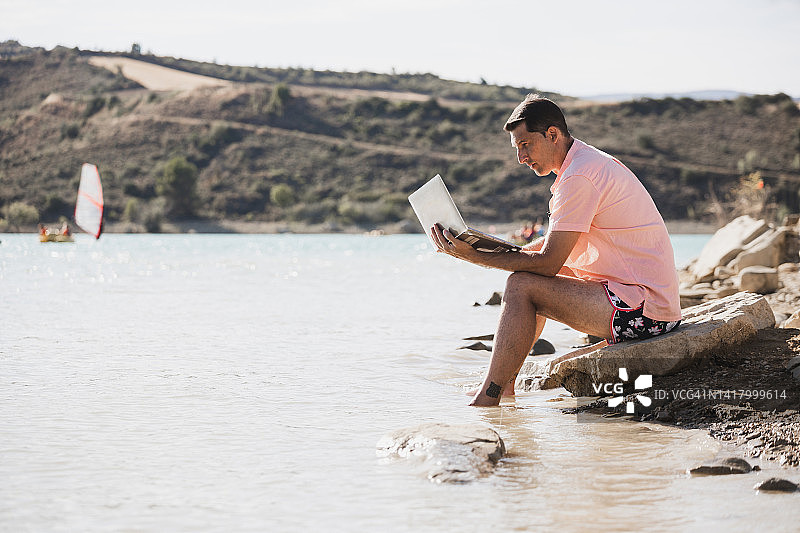 年轻男人远程办公，在湖岸边用笔记本电脑工作图片素材