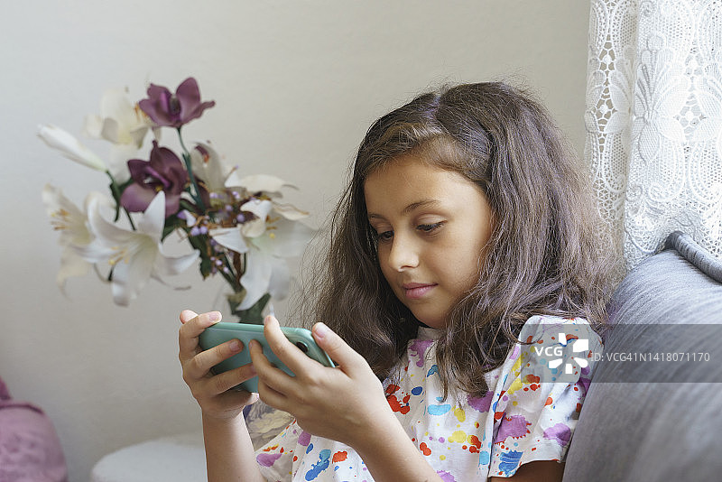 可爱的小女孩在家玩智能手机图片素材