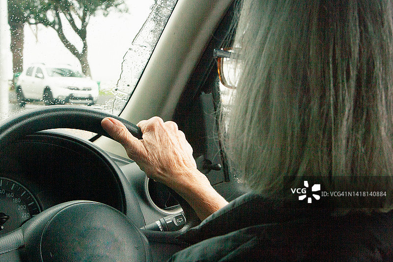 一位银发短发的老年妇女忙碌地开车，处理日常事务，她手握方向盘，眼睛注视着前方图片素材