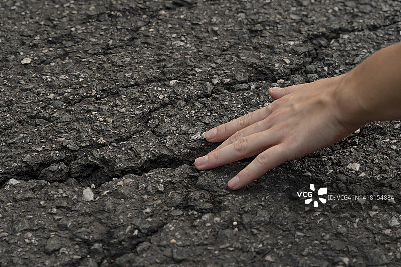 沥青路面上人手大小的裂缝。一名女子将手指伸入地面上的巨大裂缝中，道路表面运行造成的缺陷。图片素材