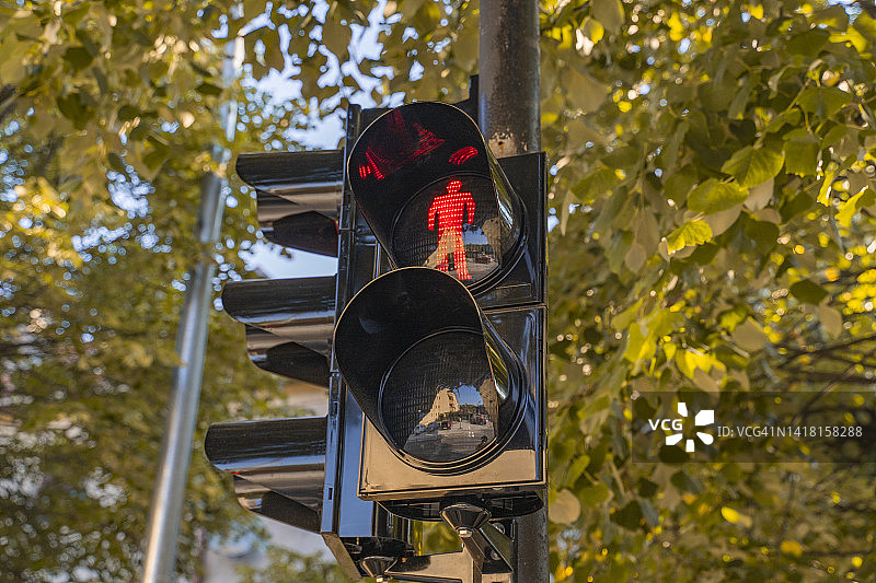 城市中的黑色交通灯显示禁止行人通行的信号，背景是橙色的秋叶。交通规则特写图片素材