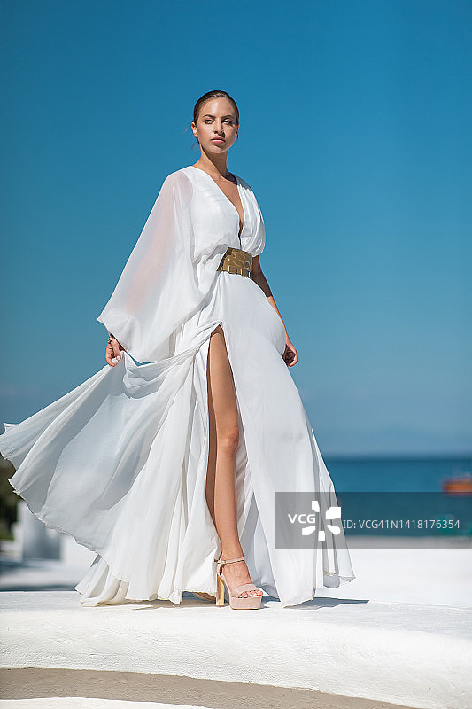 在码头上行走的系金色腰带的穿白色无袖长裙的美丽年轻女人图片素材