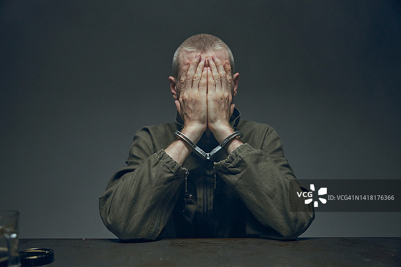 囚犯坐在桌旁，双手捂面，灰色背景图片素材