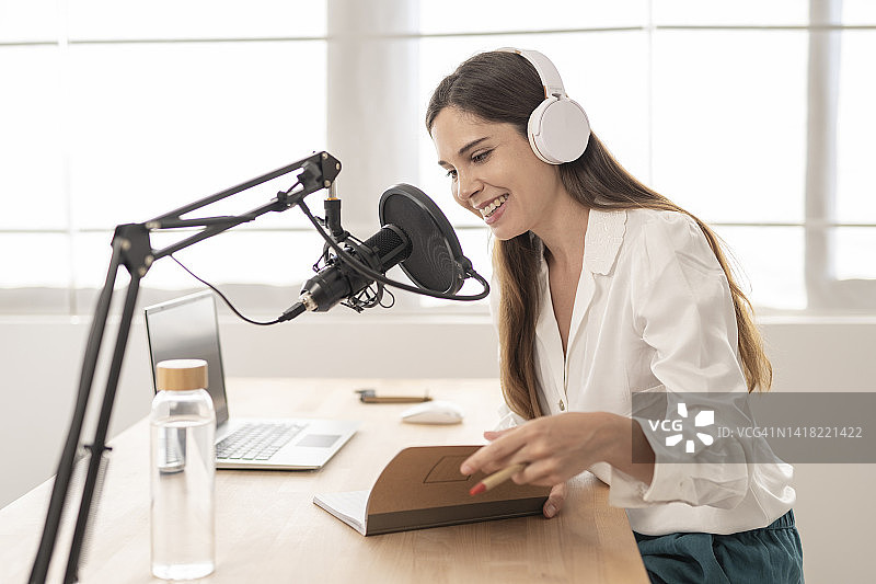 年轻女人坐在桌旁，一边录制播客一边看着笔记本图片素材