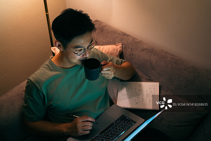 成年学生翻译在家中客厅夜间上网课并喝咖啡图片素材