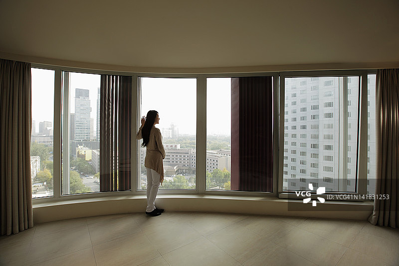 年轻女子在高层公寓的大窗户前眺望图片素材