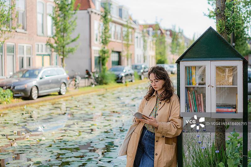 女人在街头图书漂流架旁读书图片素材