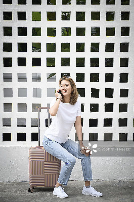 坐在行李箱上使用手机的年轻女学生图片素材