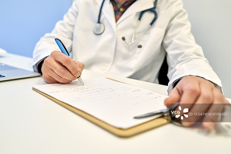 年长的医生坐着开处方药和体检的低角度视图图片素材
