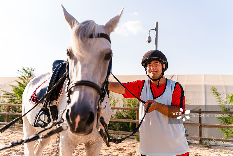 快乐的患有唐氏综合症的年轻男人爱抚着马图片素材
