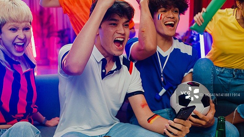一群快乐的亚洲青少年晚上坐在沙发上看足球世界杯比赛图片素材
