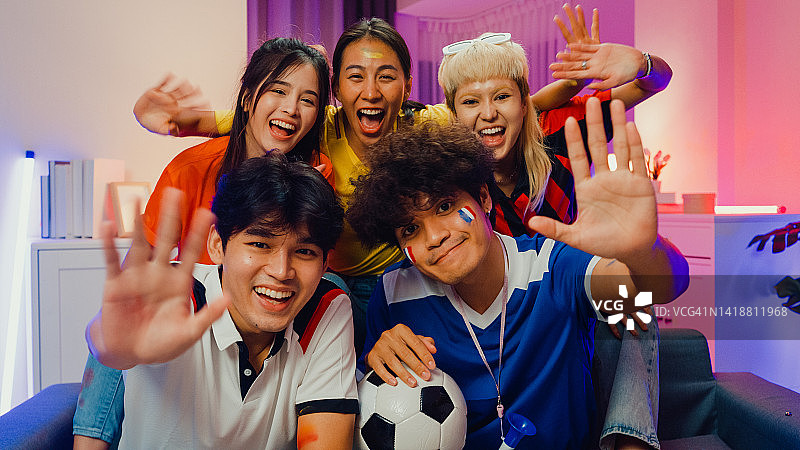 一群快乐的亚洲青少年在沙发上看着镜头进行在线视频通话，邀请朋友们一起观看足球比赛，欢笑雀跃图片素材
