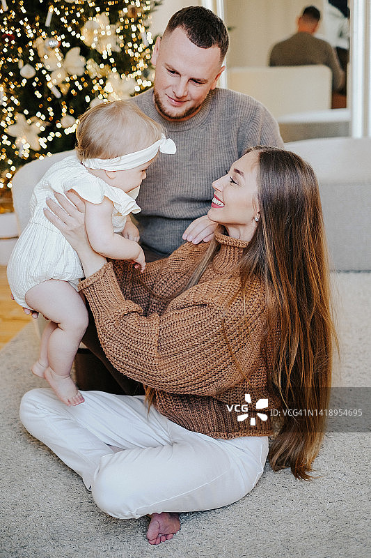 幸福的年轻家庭圣诞肖像：妈妈、爸爸和一岁的女儿在圣诞室内玩耍，家庭和圣诞节概念图片素材