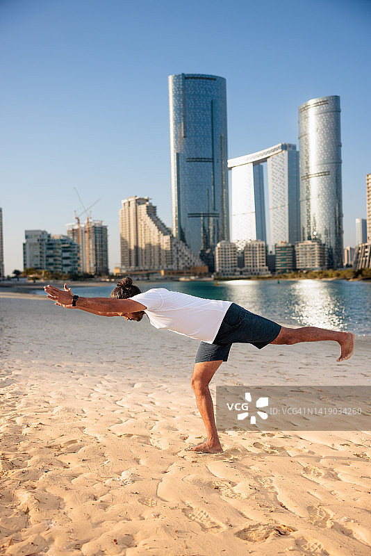 男子在阿布扎比海滩做瑜伽前倾图片素材