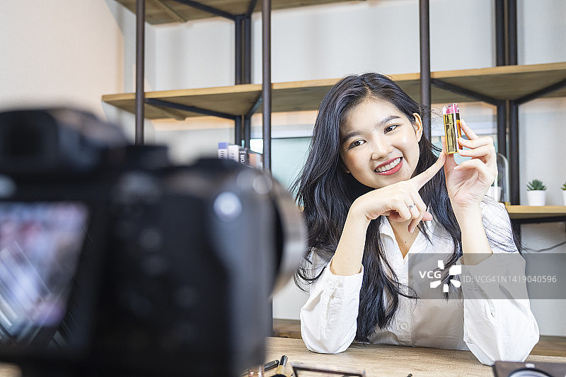 年轻漂亮的女子在镜头前展示彩妆盘并录制视频，Vlog和博客概念图片素材