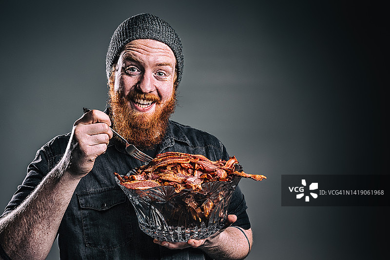 用叉子吃一碗培根的络腮胡男人图片素材