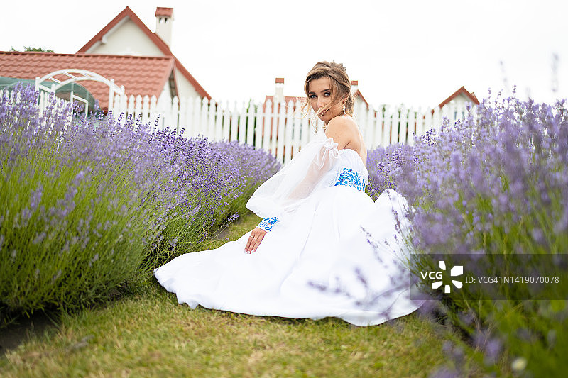 白裙少女坐在薰衣草花田中，长长的卷发，灿烂的笑容图片素材