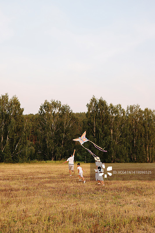 亚洲混合种族家庭在户外森林的田野里和两个孩子一起放风筝图片素材