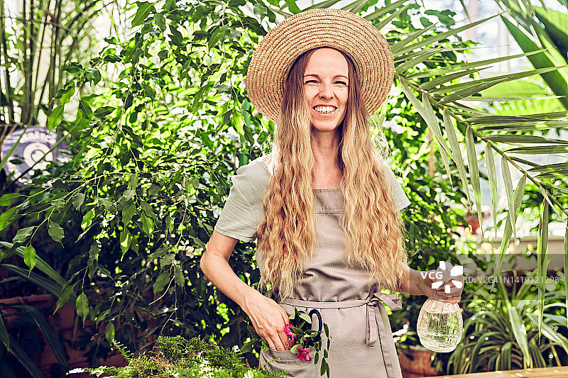 年轻女园丁在温室里喷洒植物。植物园里的晴朗的一天。图片素材