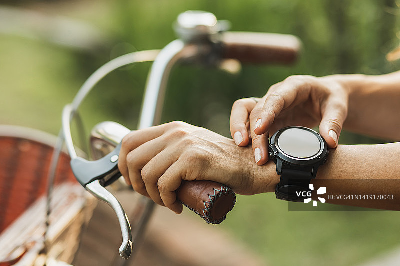 女子按下智能手表上的按钮以启动骑自行车应用程序。运动中的小工具。无法辨认的人图片素材